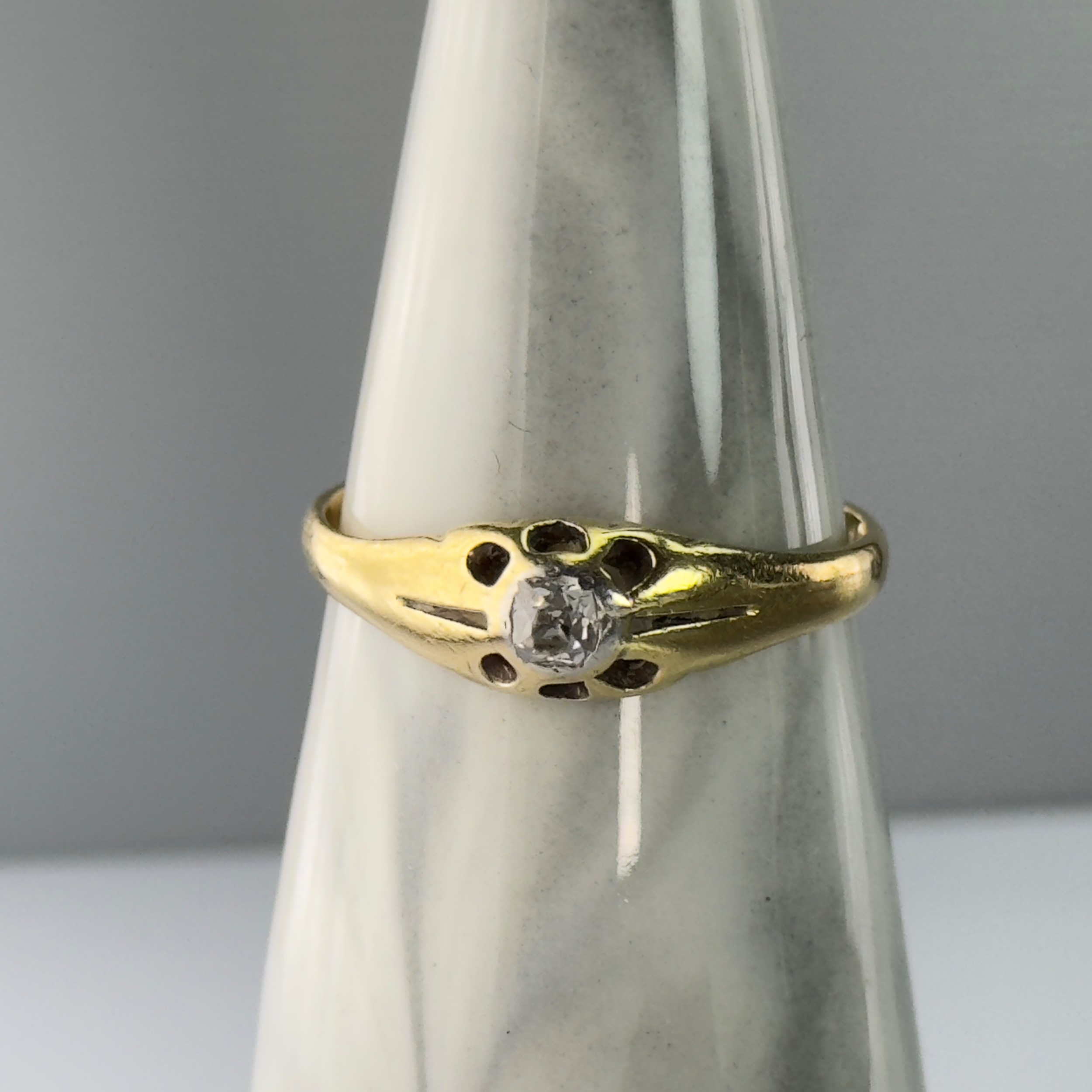 An Edwardian 18ct yellow gold solitaire ring featuring a round central diamond set within a carved starburst mount.