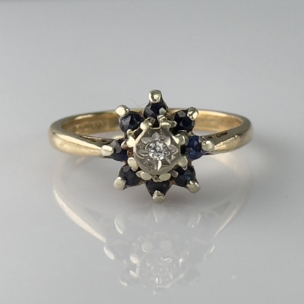 A 9ct yellow gold ring featuring a central diamond framed by a floral cluster of dark blue sapphires.