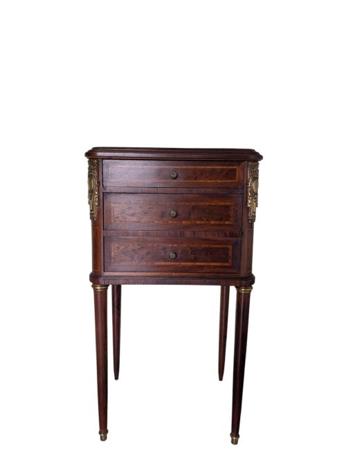 fig 1. A tall French Louis XVI style dark brown mahogany bedside cabinet featuring three drawers with decorative marquetry inlay, slender tapered legs, and ornate brass corner mounts.