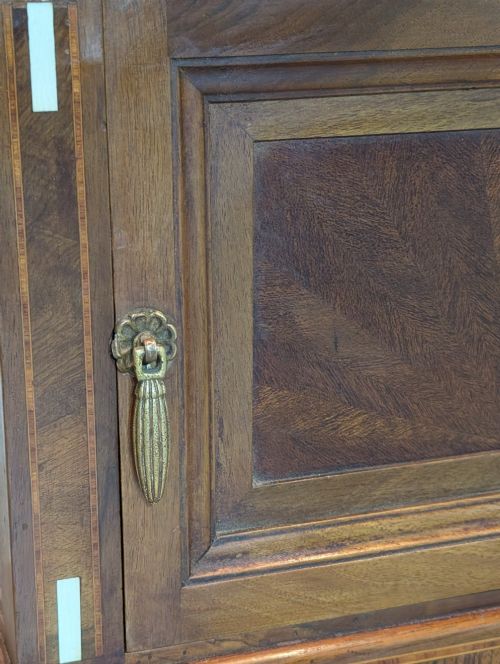 fig 2. An antique dark wood bedside cabinet featuring an open upper compartment, a lower single door cupboard with marquetry detail, white line inlays, and short curved legs.