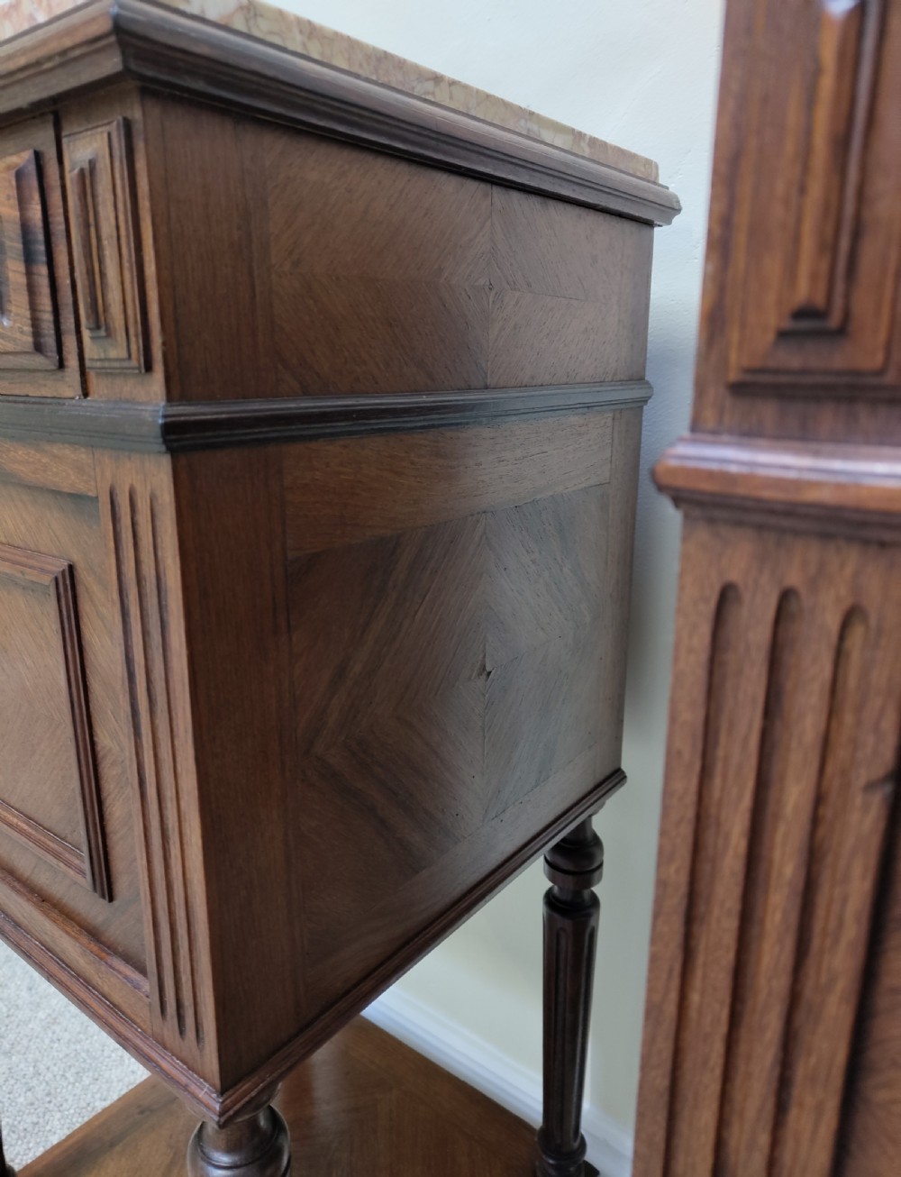 A pair of dark wood French bedside cabinets featuring carved drawer fronts, single cupboards, turned fluted legs, and variegated marble tops. View V