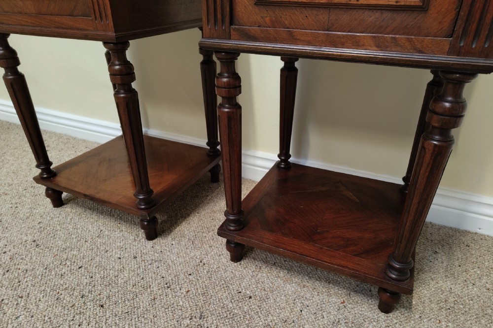 A pair of dark wood French bedside cabinets featuring carved drawer fronts, single cupboards, turned fluted legs, and variegated marble tops. View VI