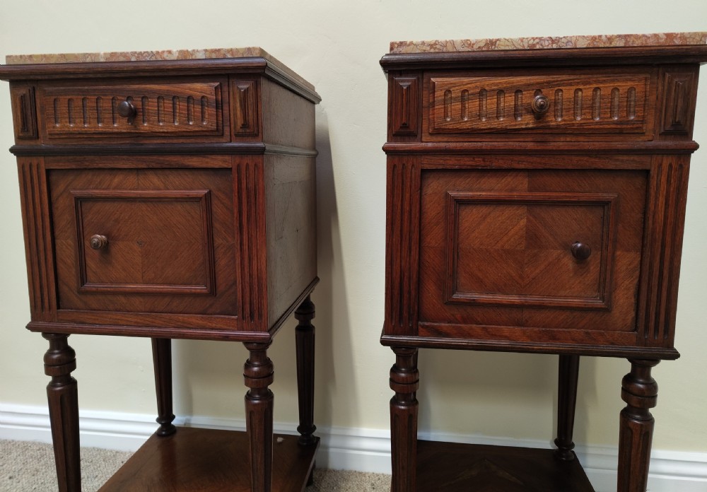 A pair of dark wood French bedside cabinets featuring carved drawer fronts, single cupboards, turned fluted legs, and variegated marble tops. View VII