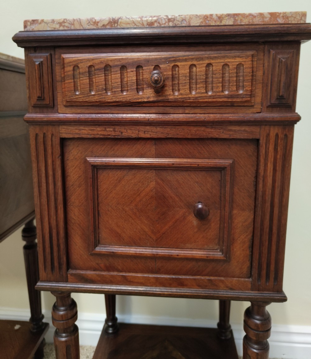 A pair of dark wood French bedside cabinets featuring carved drawer fronts, single cupboards, turned fluted legs, and variegated marble tops. View VIII