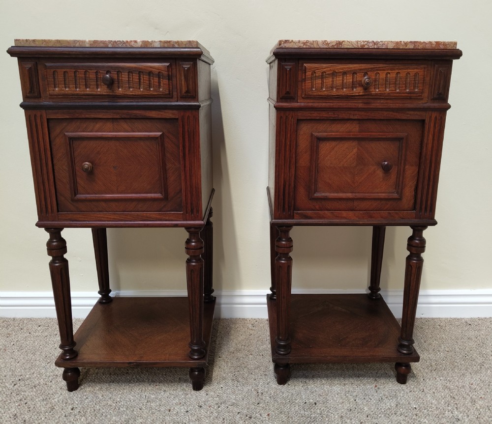 A pair of dark wood French bedside cabinets featuring carved drawer fronts, single cupboards, turned fluted legs, and variegated marble tops. View XI