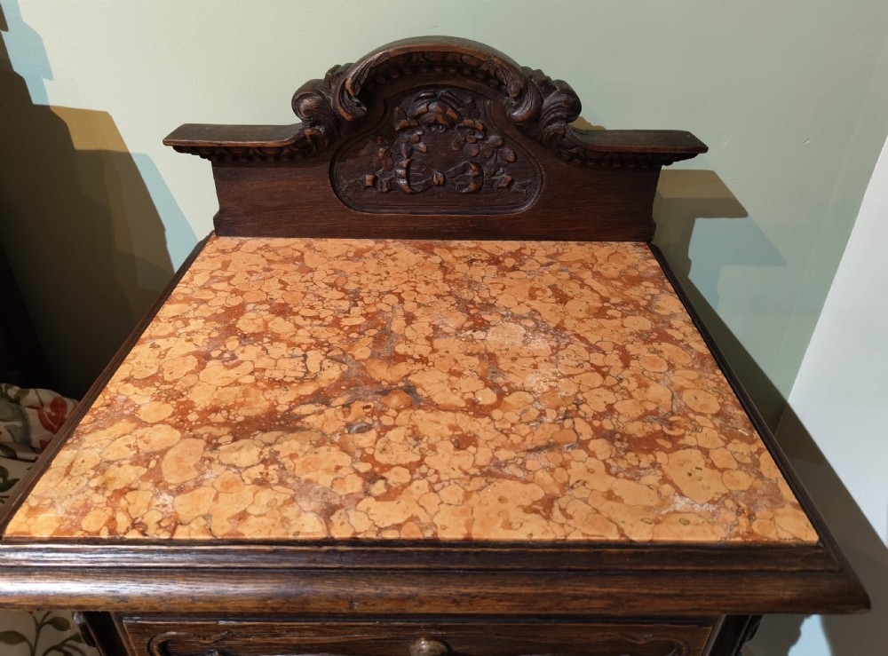 A dark oak French provincial bedside cabinet featuring a carved pediment top, a single drawer, a carved door cupboard, slender cabriole legs, and an open lower shelf. View II