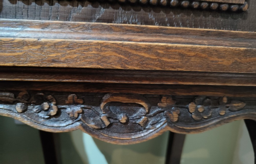 A dark oak French provincial bedside cabinet featuring a carved pediment top, a single drawer, a carved door cupboard, slender cabriole legs, and an open lower shelf. View V