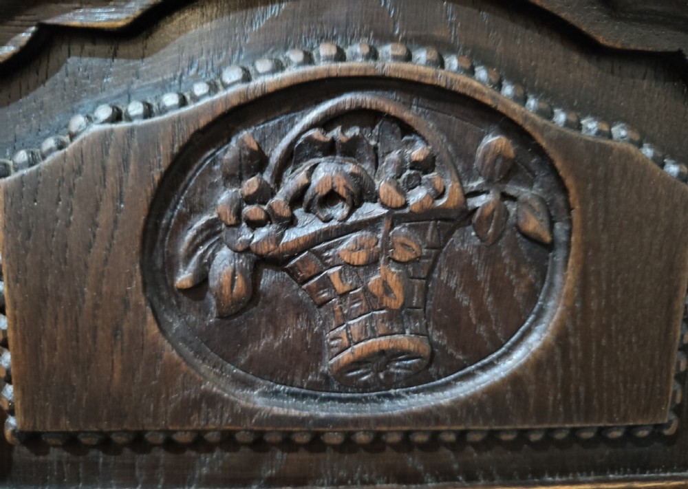 A dark oak French provincial bedside cabinet featuring a carved pediment top, a single drawer, a carved door cupboard, slender cabriole legs, and an open lower shelf. View VI