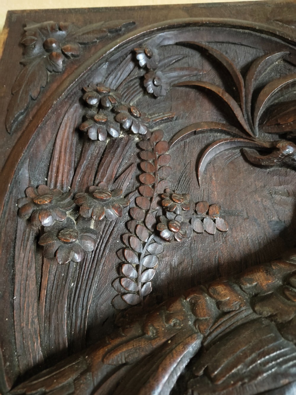 A rectangular dark wood panel featuring a high-relief carving of a bird surrounded by foliage within an oval frame. View IV
