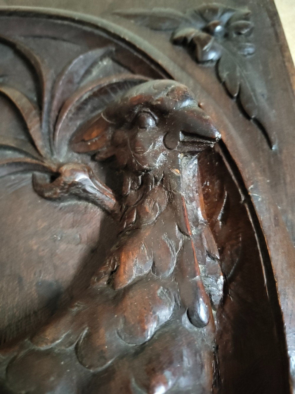 A rectangular dark wood panel featuring a high-relief carving of a bird surrounded by foliage within an oval frame. View VI