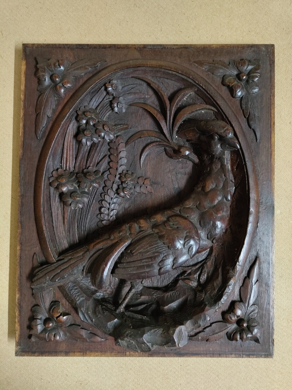 A rectangular dark wood panel featuring a high-relief carving of a bird surrounded by foliage within an oval frame. View VII