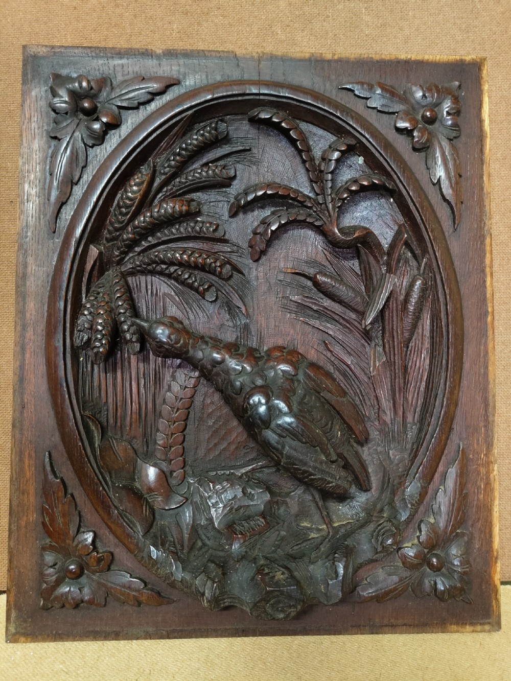A rectangular dark wood panel featuring a high-relief carving of a bird surrounded by foliage within an oval frame. View VIII