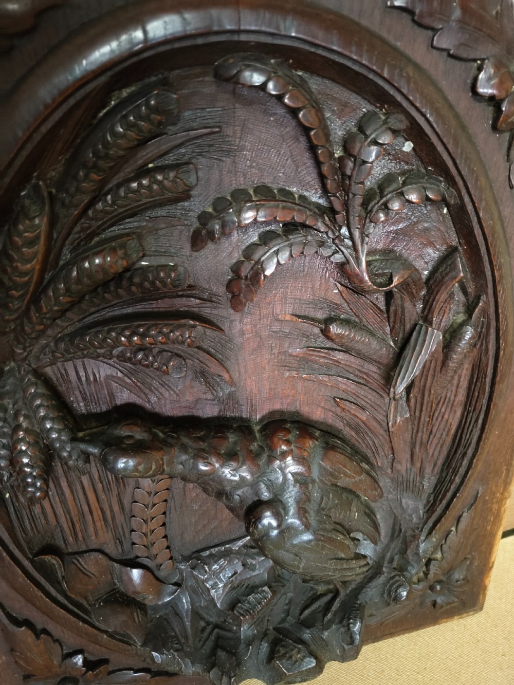 A rectangular dark wood panel featuring a high-relief carving of a bird surrounded by foliage within an oval frame. View IX
