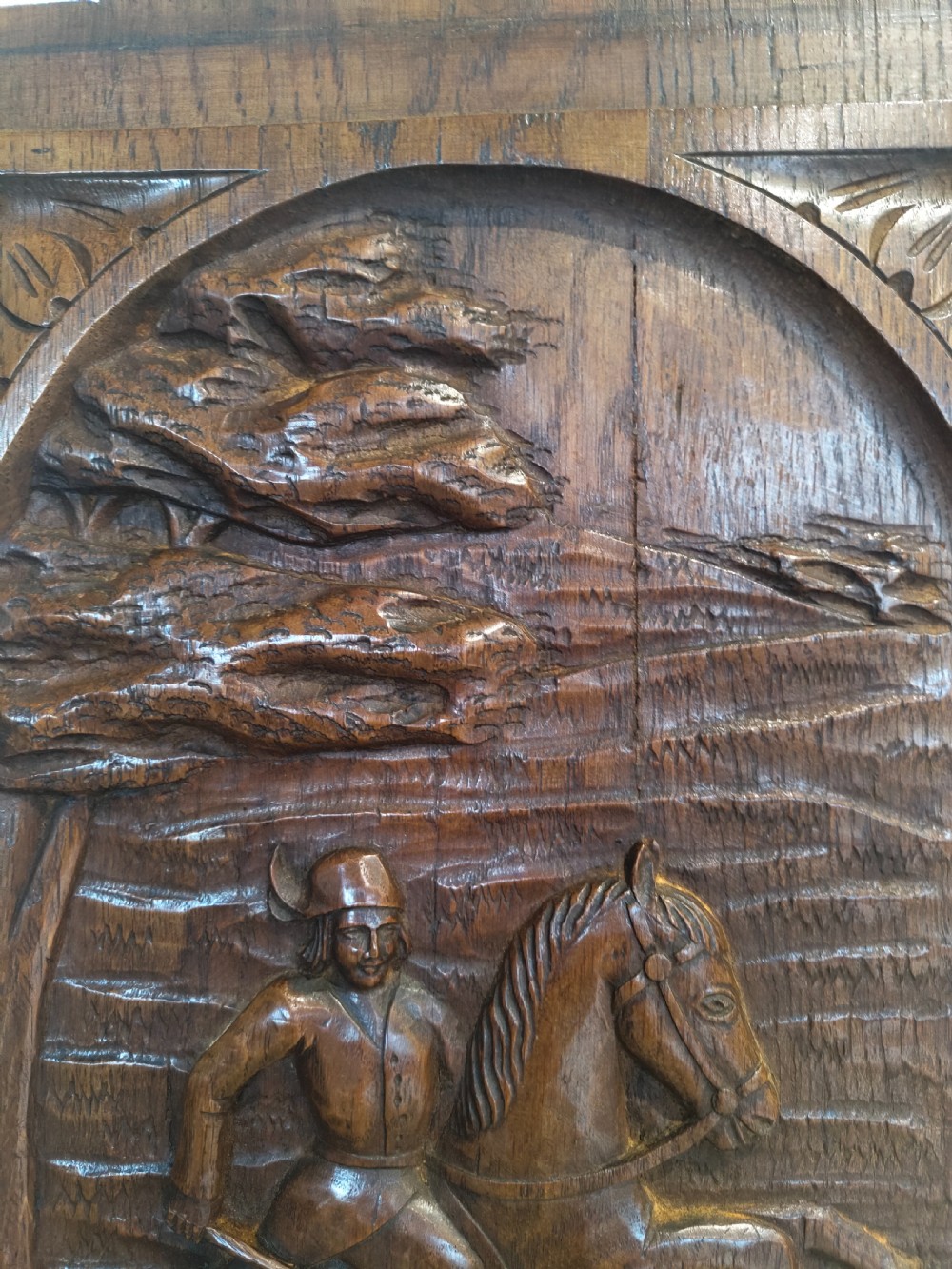 A dark brown carved oak rectangular panel depicting a high-relief equestrian hunting scene framed within an arched border. View II