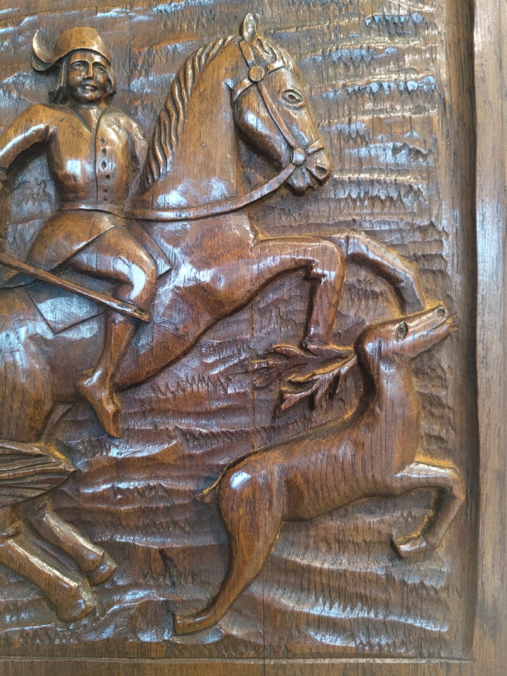 A dark brown carved oak rectangular panel depicting a high-relief equestrian hunting scene framed within an arched border. View III