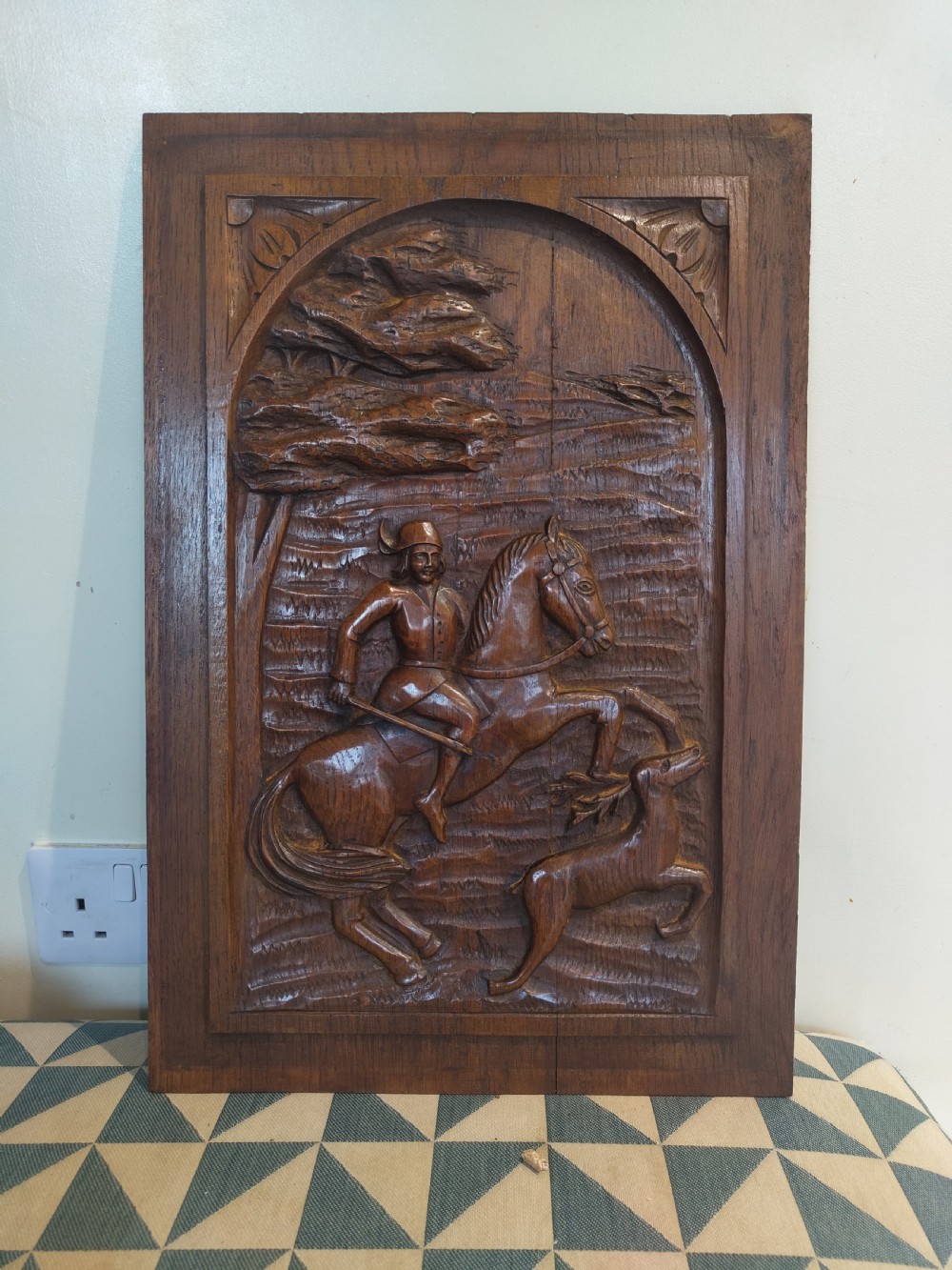 A dark brown carved oak rectangular panel depicting a high-relief equestrian hunting scene framed within an arched border. View V