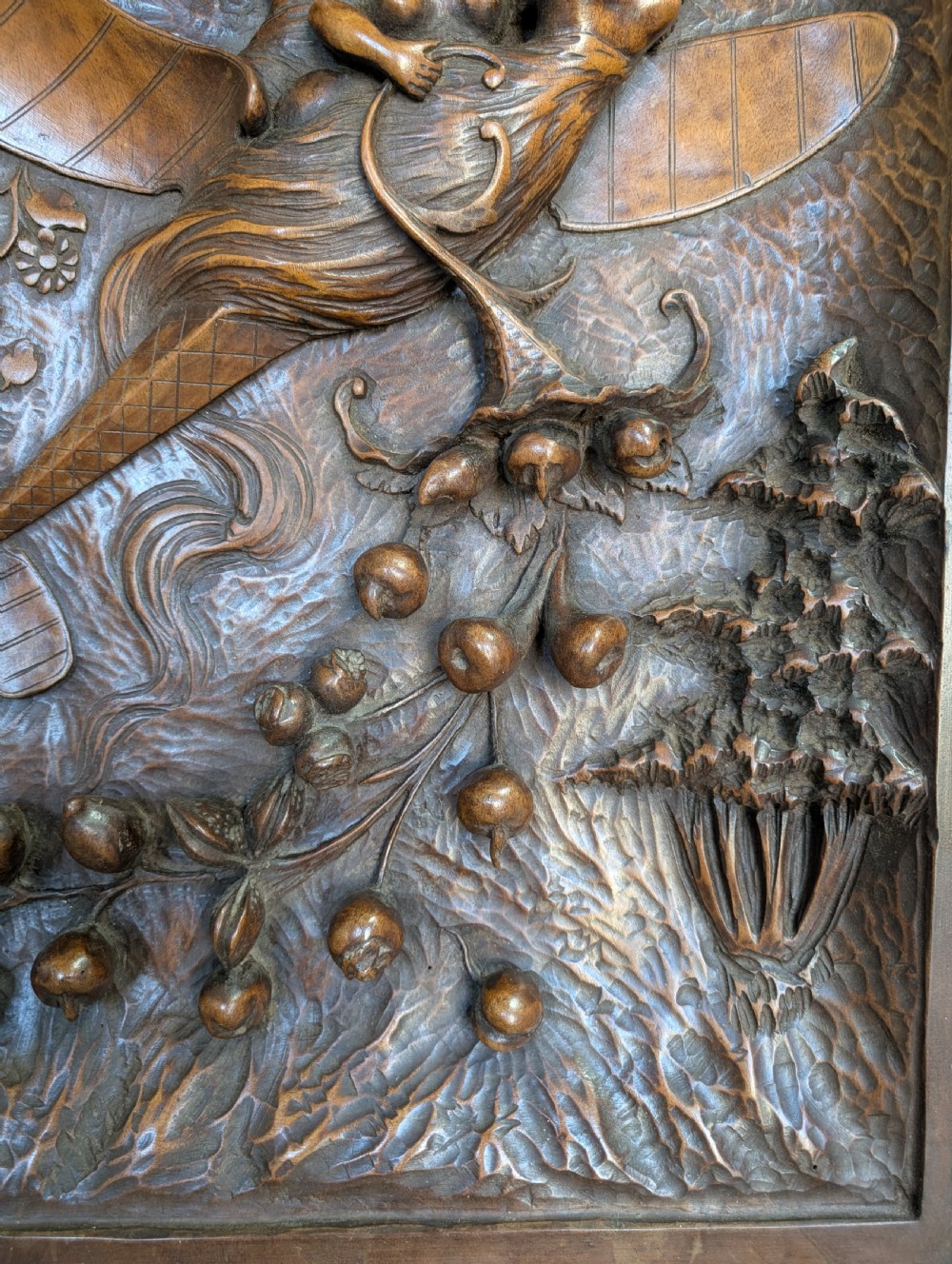 An arched carved wood wall panel featuring high-relief details of figures on a flying vessel, an eagle, a sun, and botanical elements in a warm brown finish. View V