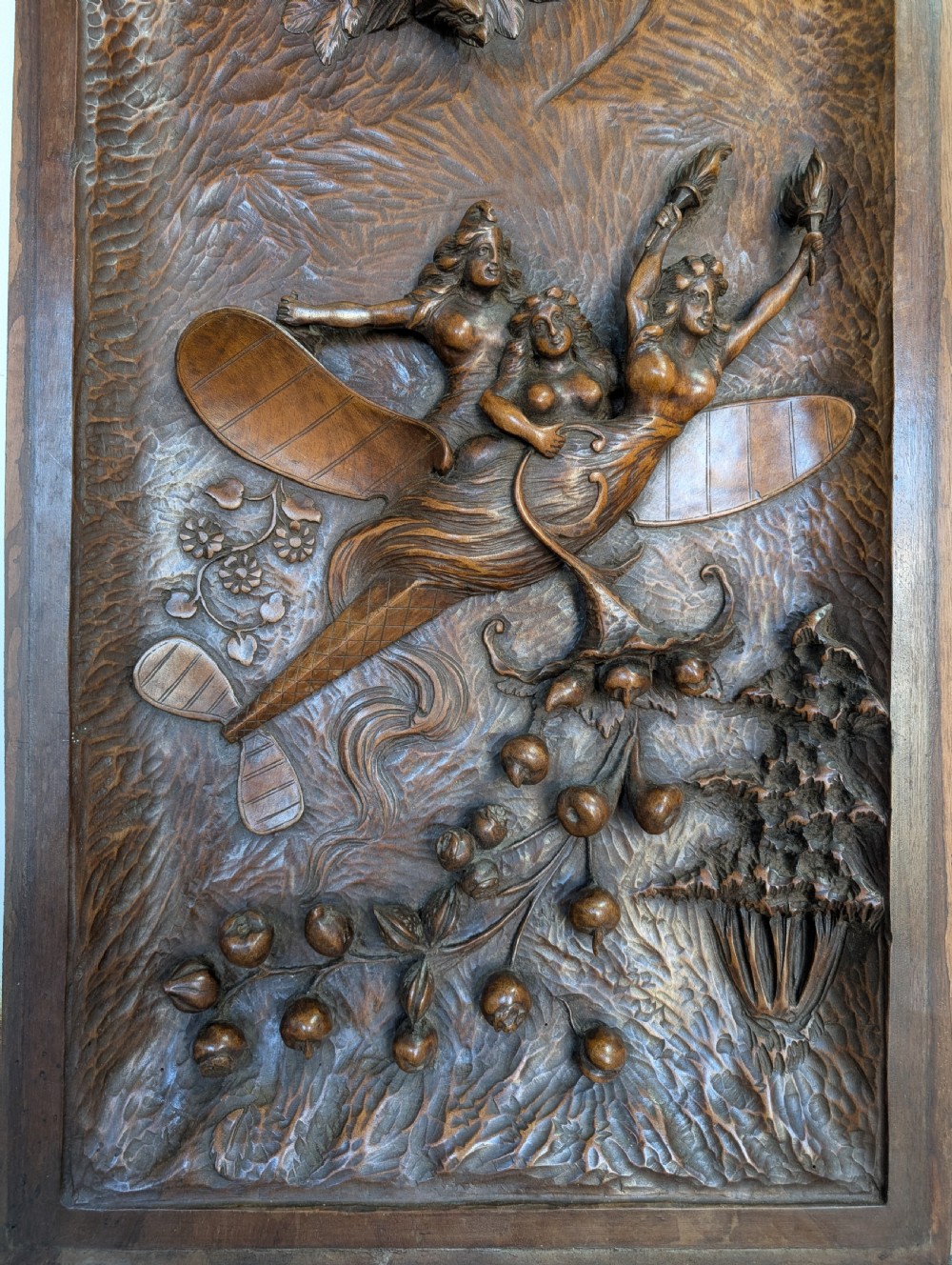 An arched carved wood wall panel featuring high-relief details of figures on a flying vessel, an eagle, a sun, and botanical elements in a warm brown finish. View VIII