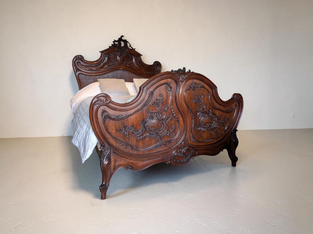 An antique French Rococo Revival style carved walnut bed featuring serpentine shaping, relief floral carvings, and a contoured headboard and footboard. View XXI