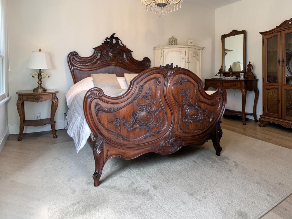 An antique French Rococo Revival style carved walnut bed featuring serpentine shaping, relief floral carvings, and a contoured headboard and footboard. View XXIII