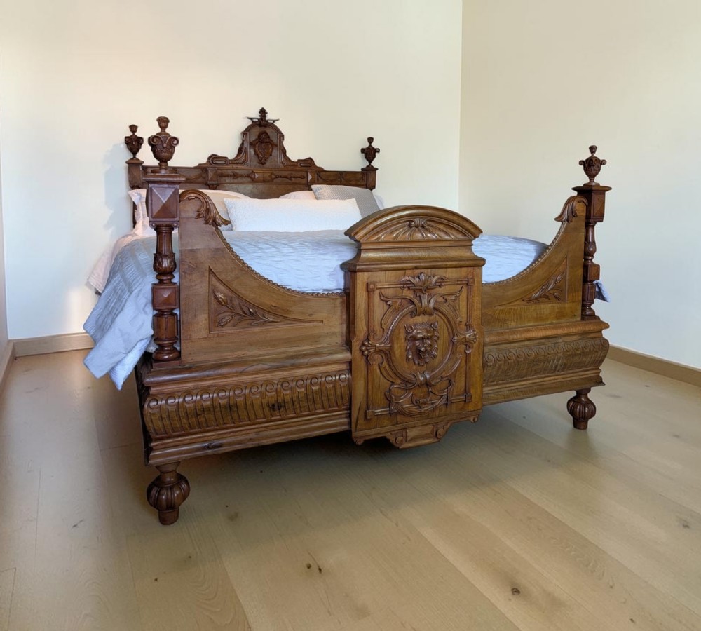 An antique super king size carved wooden bedstead with turned finials and a central relief carving of a lion mask on the footboard.