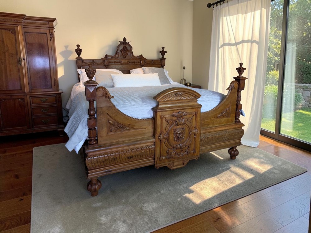 An antique super king size carved wooden bedstead with turned finials and a central relief carving of a lion mask on the footboard. View II