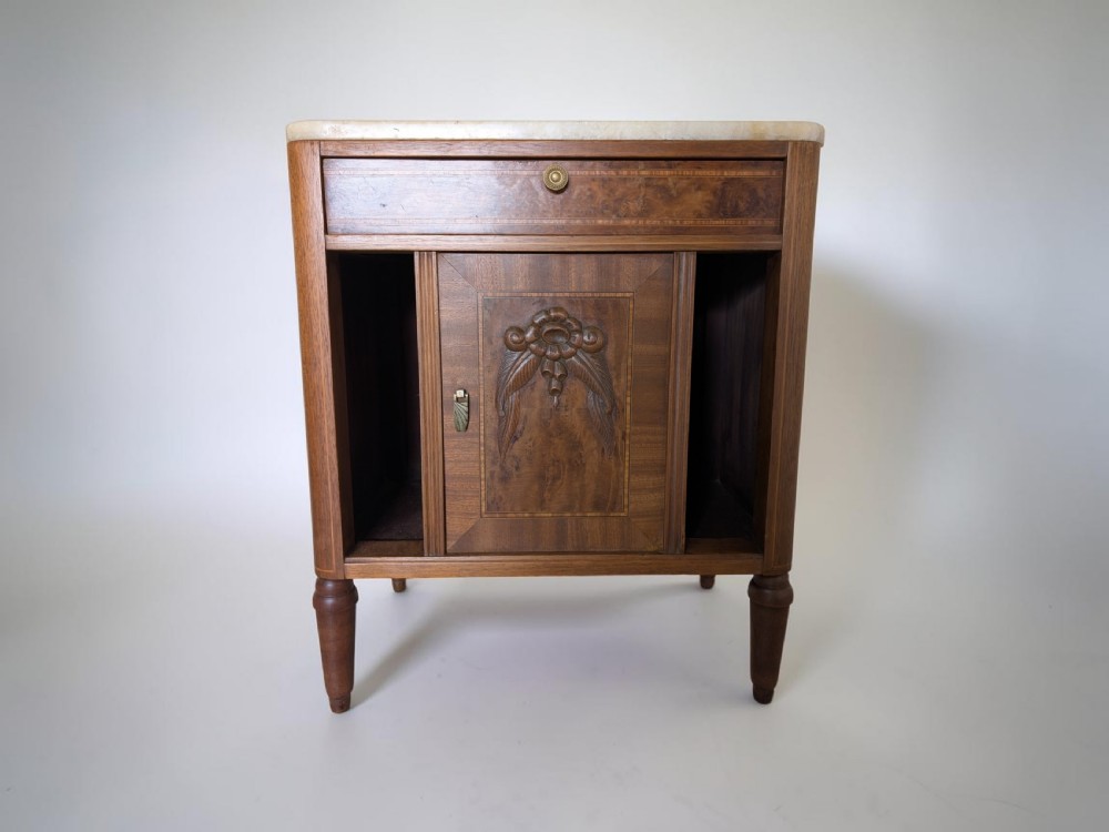 An antique walnut bedside cabinet featuring a pale marble top, central carved cupboard door, single drawer, open side compartments, and tapered legs.
