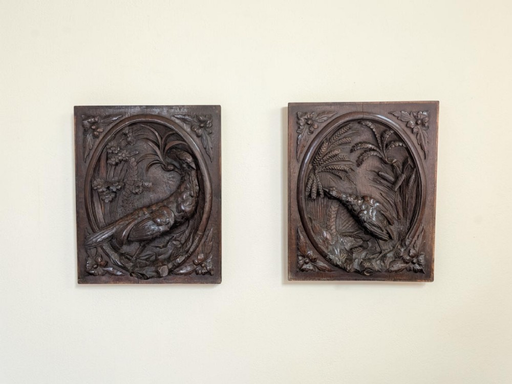 A rectangular dark wood panel featuring a high-relief carving of a bird surrounded by foliage within an oval frame.