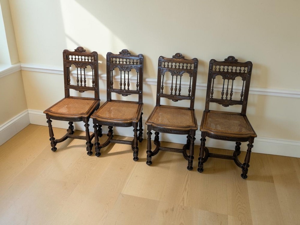 A set of four antique dark carved oak dining chairs featuring openwork spindle backs and woven cane seats.