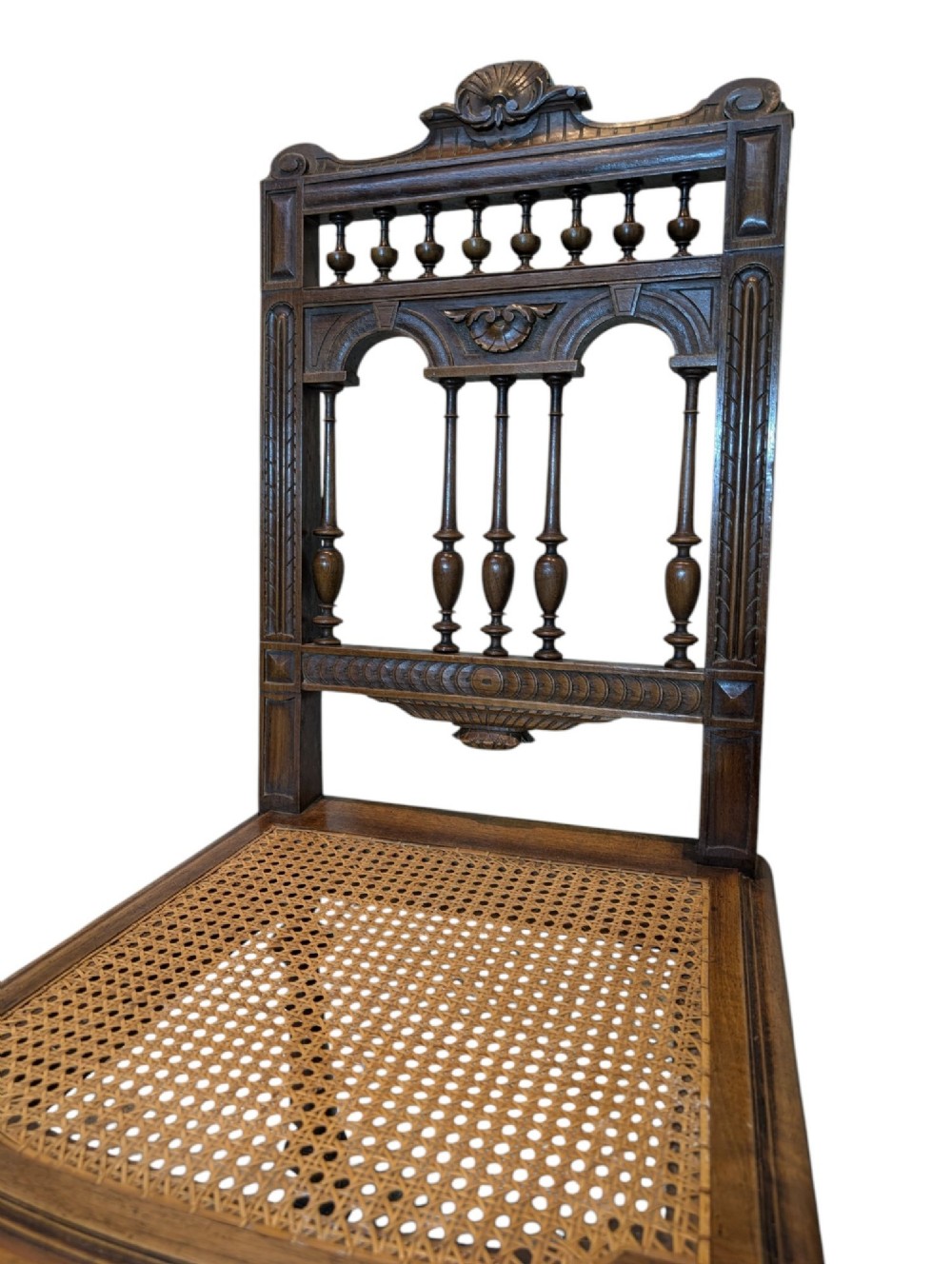 A set of four antique dark carved oak dining chairs featuring openwork spindle backs and woven cane seats. View IV