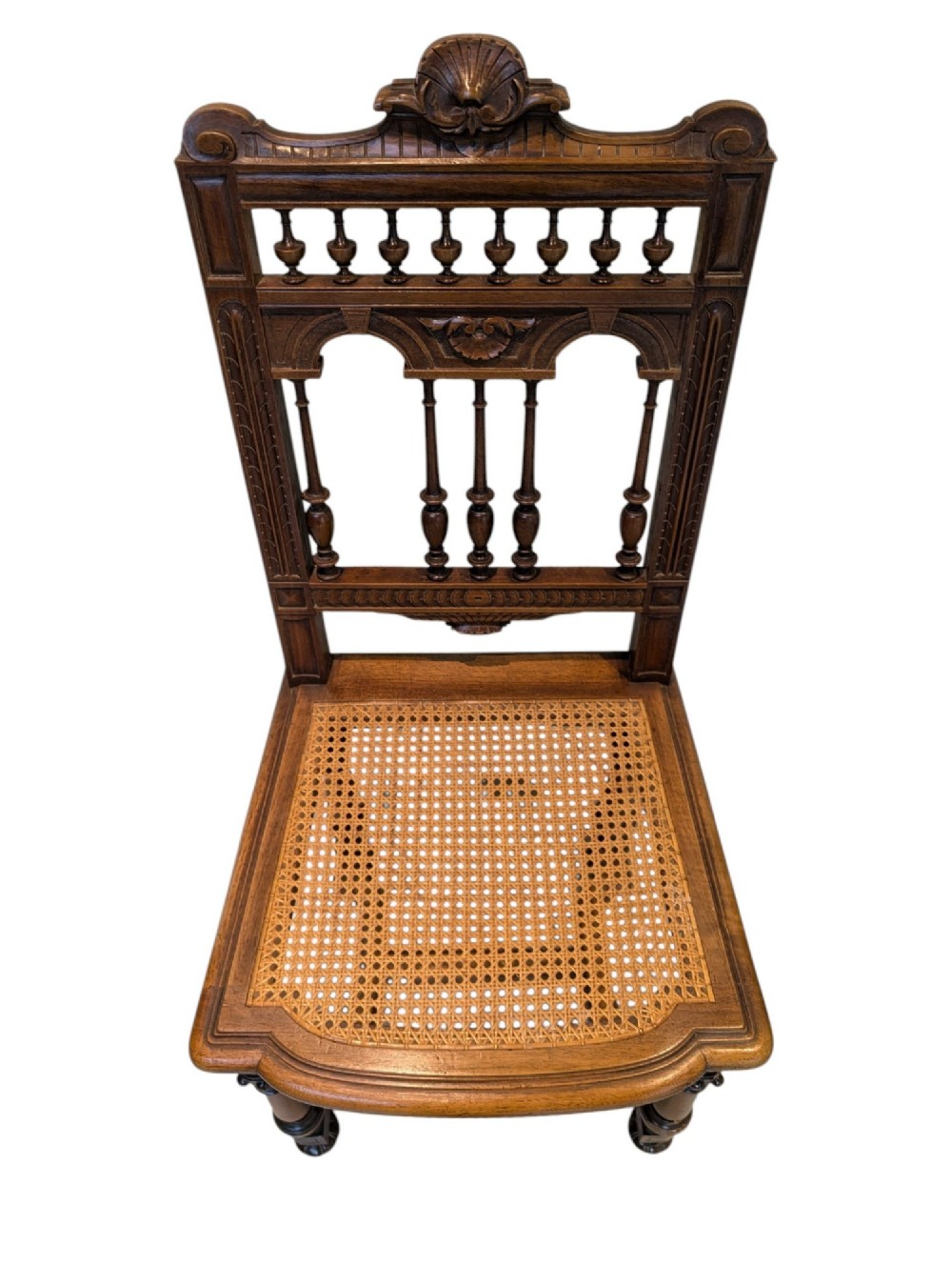 A set of four antique dark carved oak dining chairs featuring openwork spindle backs and woven cane seats. View V