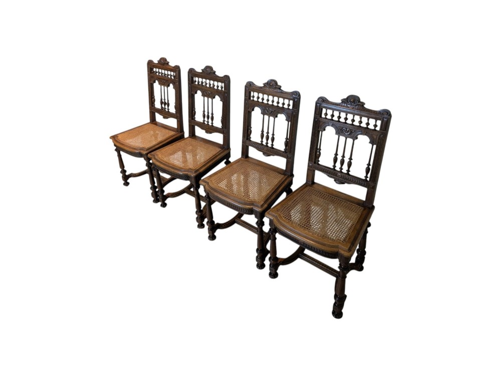 A set of four antique dark carved oak dining chairs featuring openwork spindle backs and woven cane seats. View X