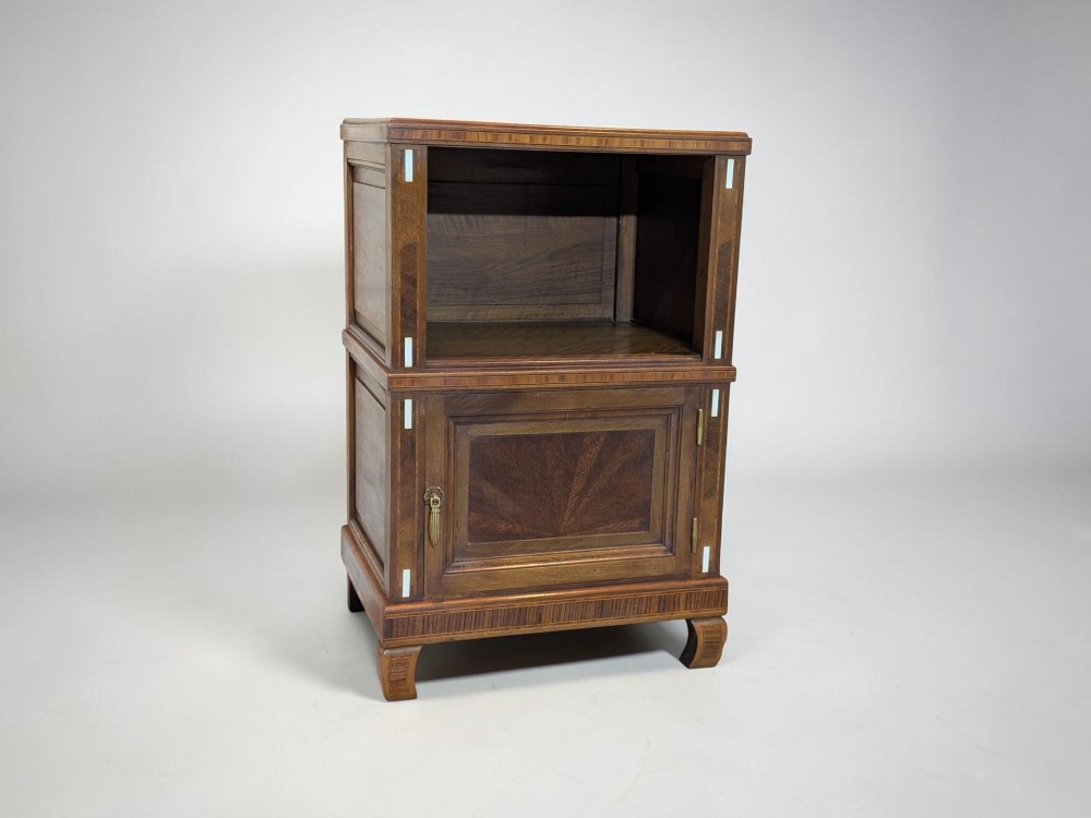 An antique dark wood bedside cabinet featuring an open upper compartment, a lower single door cupboard with marquetry detail, white line inlays, and short curved legs.