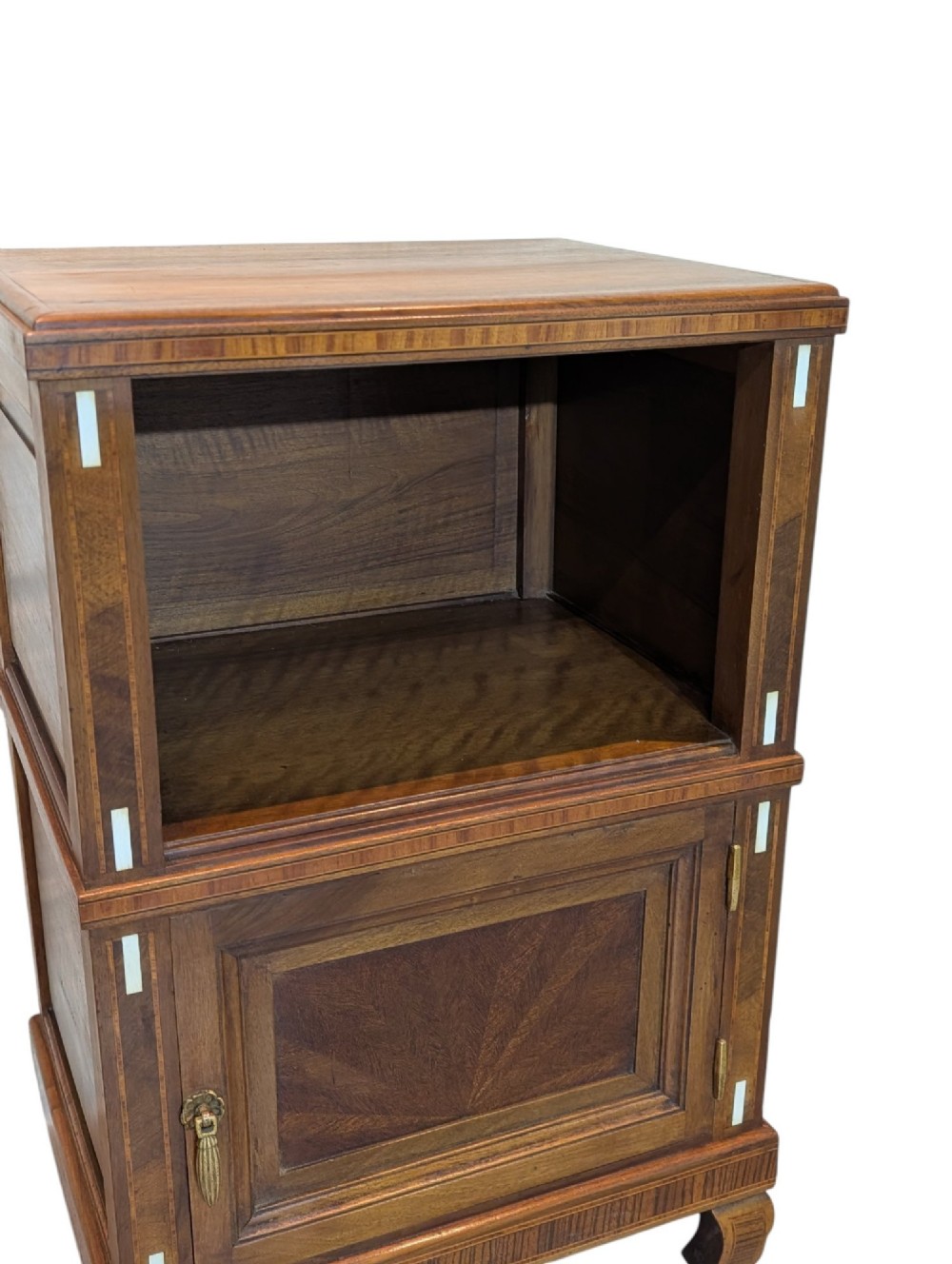 An antique dark wood bedside cabinet featuring an open upper compartment, a lower single door cupboard with marquetry detail, white line inlays, and short curved legs. View VI