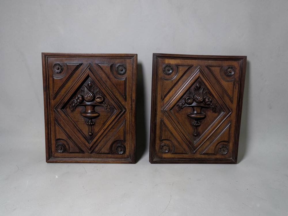 A pair of dark oak rectangular carved panels featuring central urn motifs enclosed by geometric diamond mouldings and corner floral rosettes.