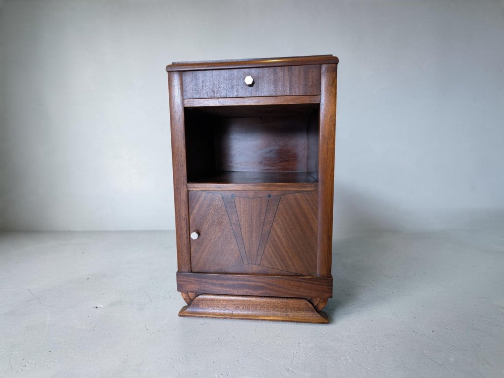 A dark brown walnut Art Deco bedside cabinet featuring a top drawer, an open central shelf, a cupboard door with geometric veneer inlay, and hexagonal metal knobs.