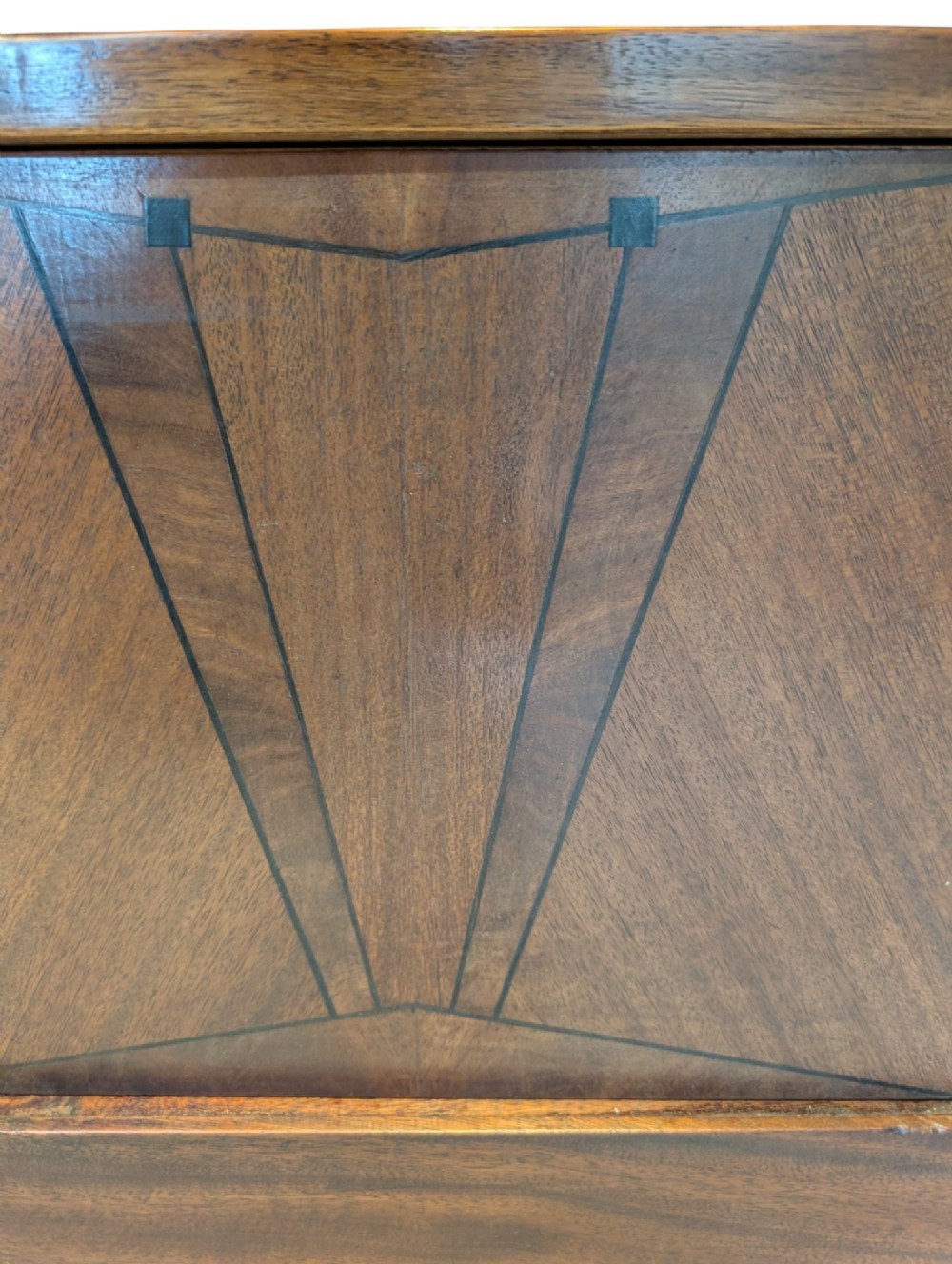 A dark brown walnut Art Deco bedside cabinet featuring a top drawer, an open central shelf, a cupboard door with geometric veneer inlay, and hexagonal metal knobs. View VII
