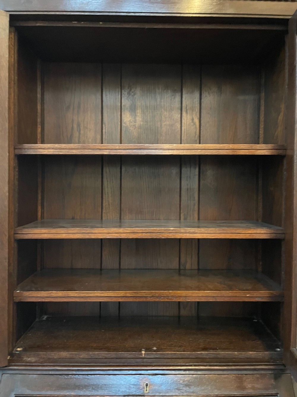 A dark oak Edwardian bureau bookcase featuring a twin-glazed door upper cabinet positioned above a slant-front writing slope and two lower drawers on turned legs. View V