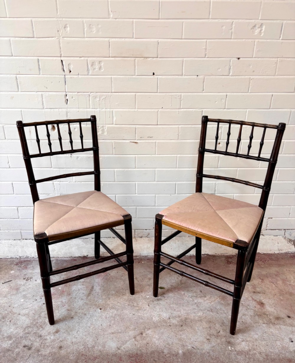 A pair of dark wood side chairs featuring turned frames imitating bamboo and light beige woven rush envelope seats.