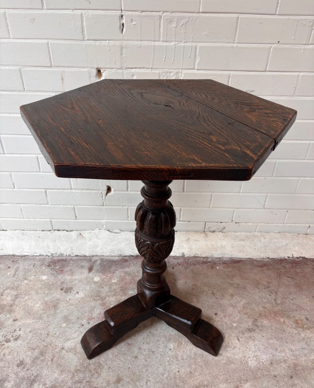 A dark oak pedestal side table featuring a hexagonal top resting on a carved central stem with tripod legs.