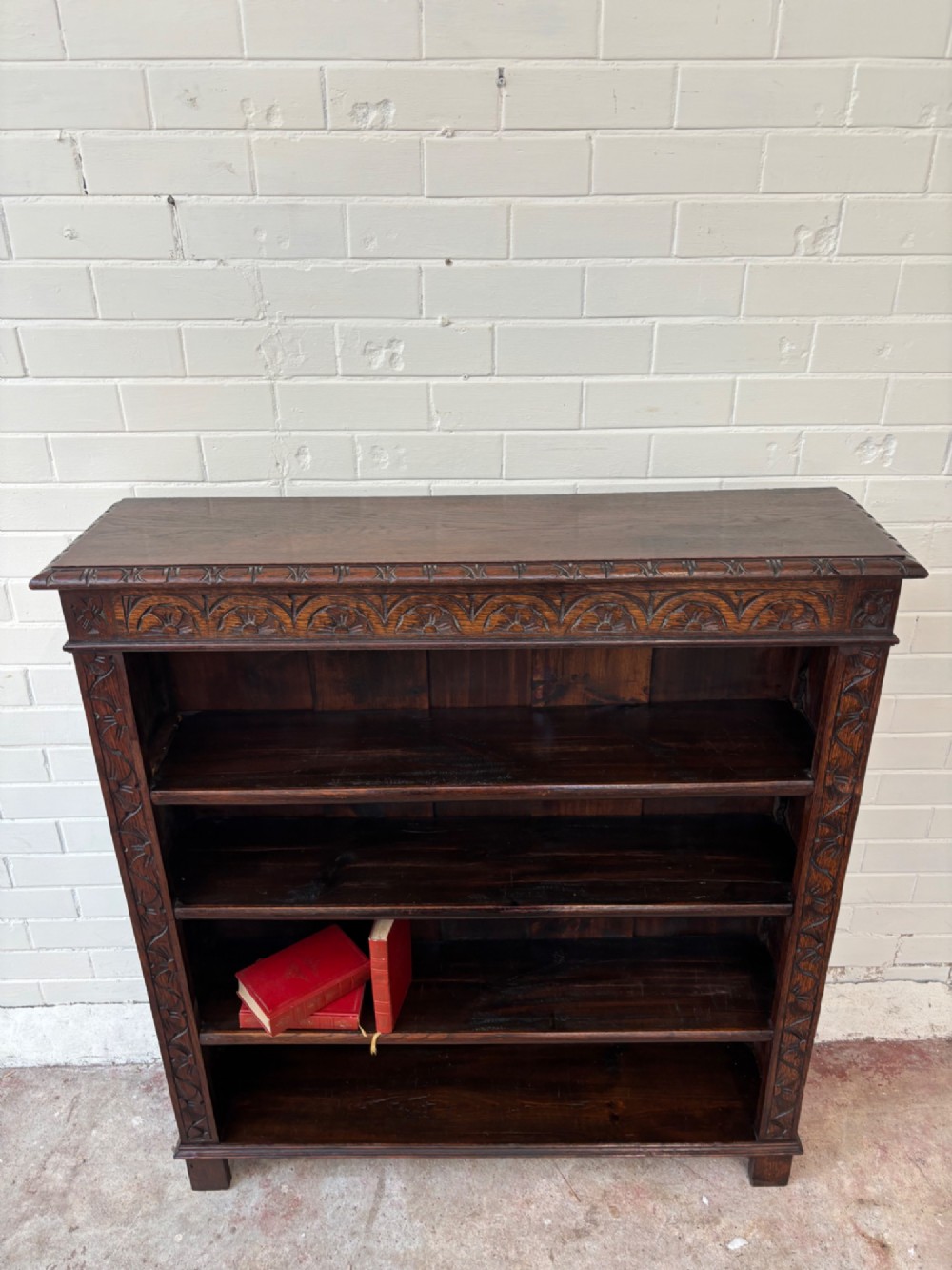 A low dark oak open bookcase featuring detailed lunette carving along the upper frieze and carved foliate borders down the upright sides. View III