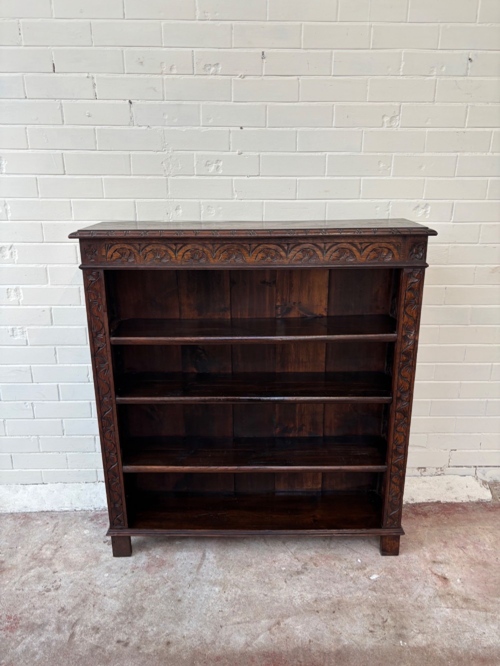 A low dark oak open bookcase featuring detailed lunette carving along the upper frieze and carved foliate borders down the upright sides. View IV