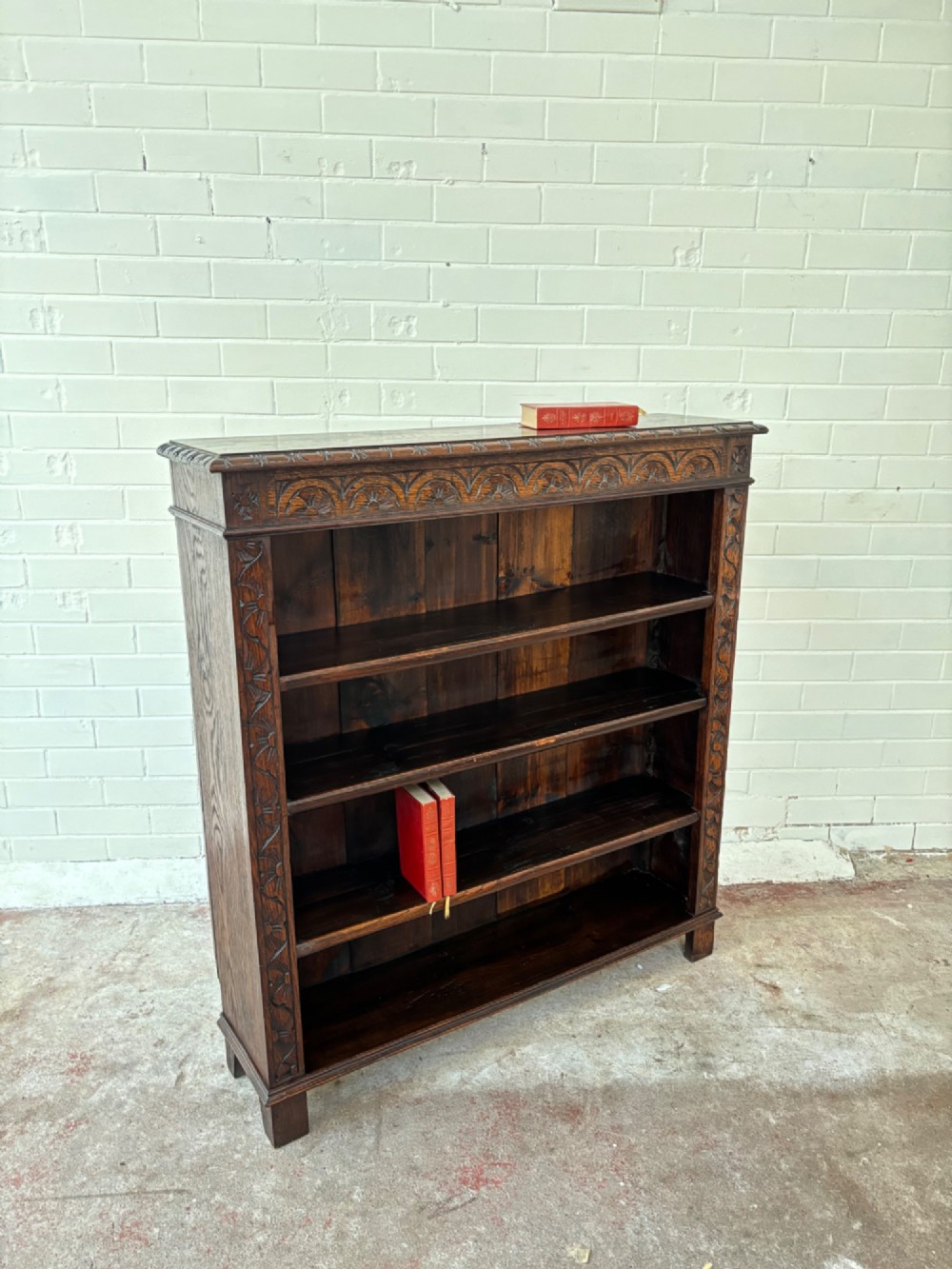 A low dark oak open bookcase featuring detailed lunette carving along the upper frieze and carved foliate borders down the upright sides. View X
