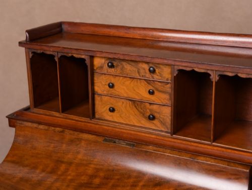 fig 2. A Victorian burr walnut pop-up Davenport desk featuring carved scroll front supports, side drawers with wooden knobs, and a hinged sloping top.