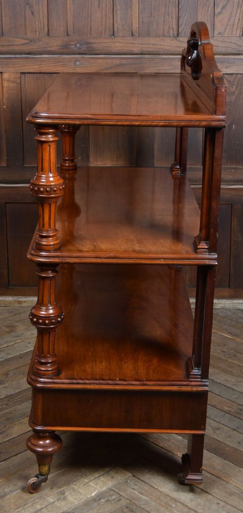 A Victorian mahogany three-tiered whatnot featuring turned column supports, two lower drawers with knob handles, an arched gallery top, and brass castors. View IX