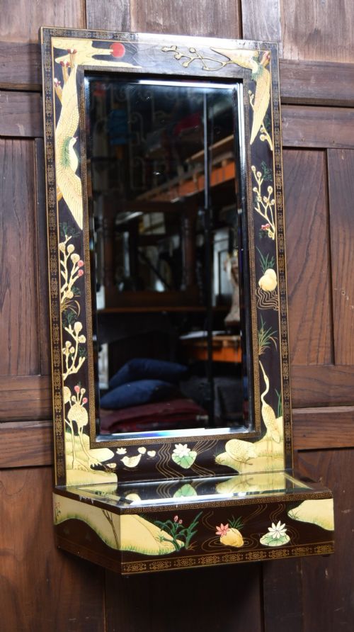 fig 1. A tall black lacquered rectangular wall mirror featuring an integrated bottom shelf and painted borders with cranes, lotus blossoms, and botanical details.