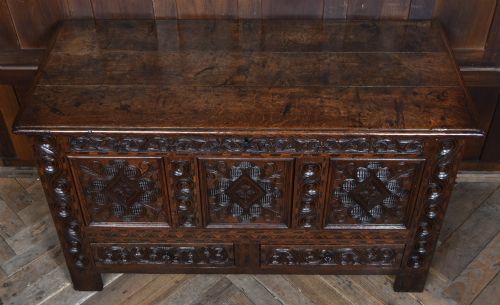 fig 1. An 18th-century dark oak coffer featuring three carved panels, geometric marquetry inlay, and two lower drawers.