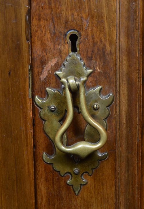 An antique Art Nouveau corner wardrobe crafted from warm walnut wood with an arched pediment, a single panel door featuring floral marquetry, and a shaped plinth base. View II