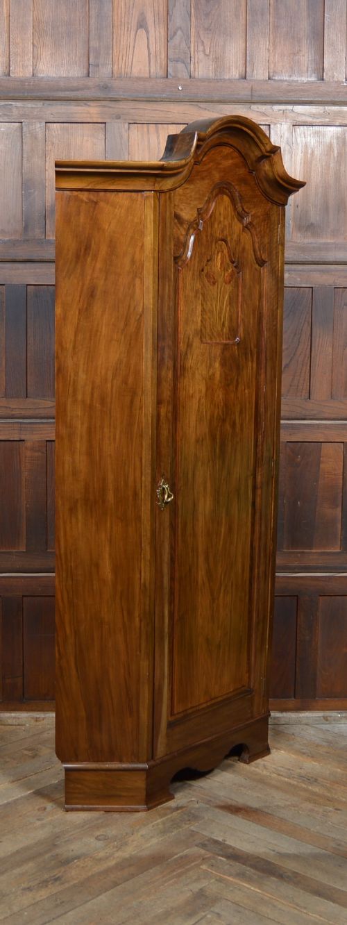 An antique Art Nouveau corner wardrobe crafted from warm walnut wood with an arched pediment, a single panel door featuring floral marquetry, and a shaped plinth base. View XII