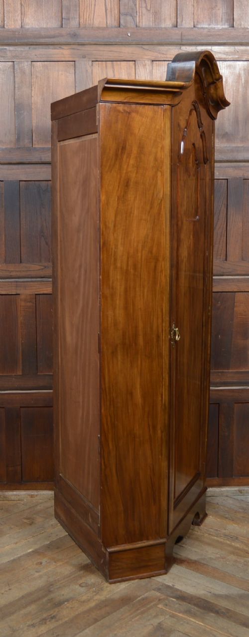 An antique Art Nouveau corner wardrobe crafted from warm walnut wood with an arched pediment, a single panel door featuring floral marquetry, and a shaped plinth base. View XIII